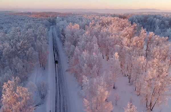 An aerial view shows a car driving along a forest road during sunset in the Siberian