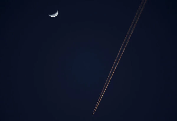 An aeroplane flies past a crescent moon at dusk in Alcala de Henares