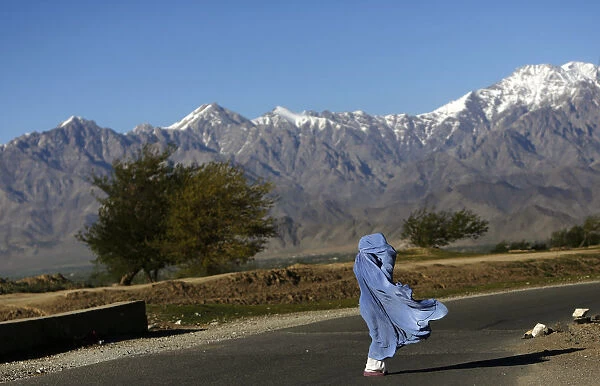 An Afghan woman in a burqa walks along a road on a windy day on the outskirts of Kabul