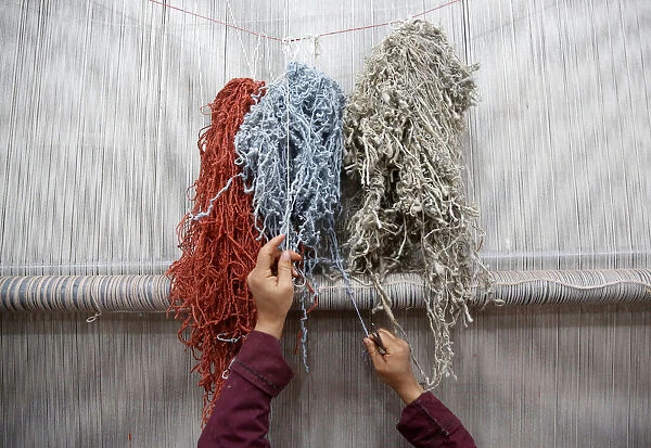 An Afghan woman reaches for a thread while working at the Afghanistan Rug