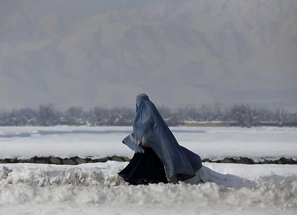An Afghan woman walks along a street covered with snow on the outskirts of Kabul