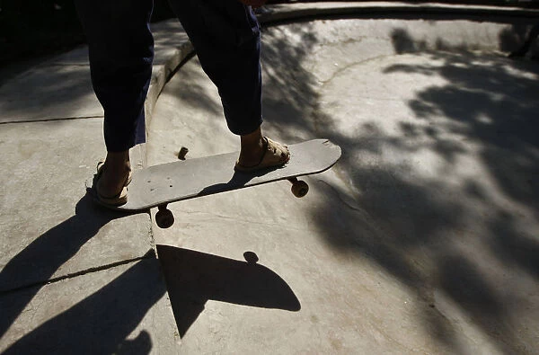 An Afghan youth prepares to ride a skateboard in a disused fountain in a Kabul park