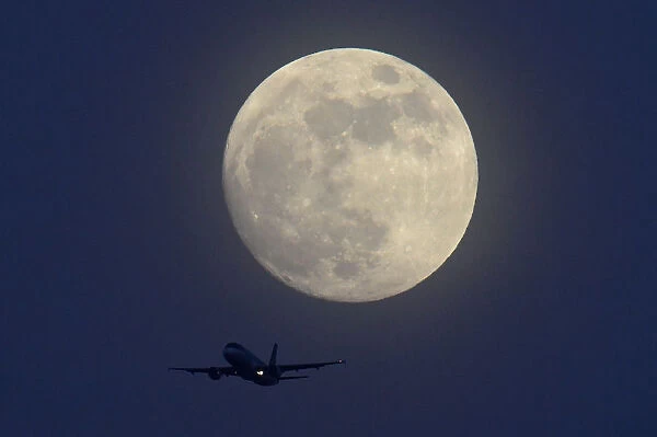 An aicraft flies infront of a full moon over London