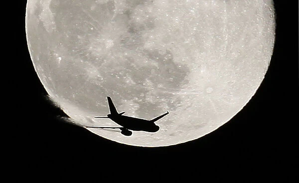 An airplane is silhouetted against a full moon in the sky over London