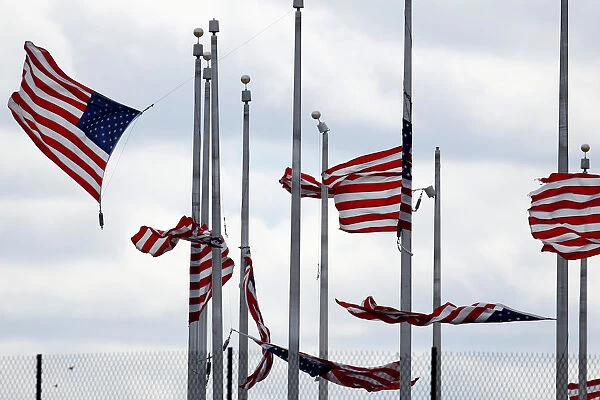 American flags partially torn from their poles fly as a storm producing strong winds