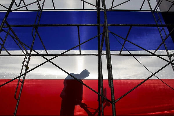 An anti-government protester casts a shadow behind a large Thai national flag during a
