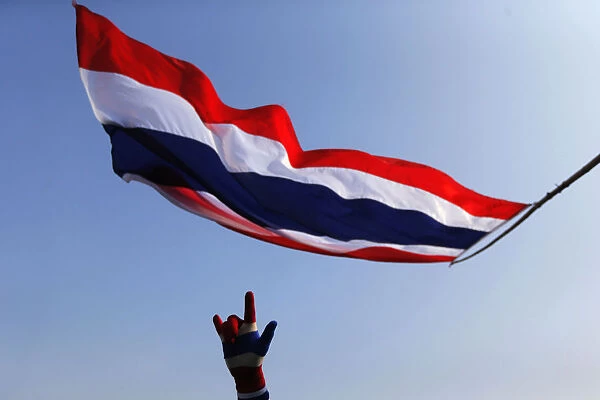 An anti-government protester gestures below a Thai national flag as he stands on a