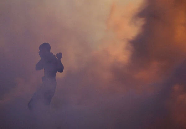 An anti-government protester runs through a cloud of tear gas holding a camera during