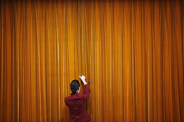 An attendant puts clamps on a curtain inside the Great Hall of the People during the