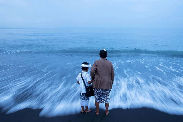 A Balinese Hindu woman hold her grandsons hand on a beach during Melasti