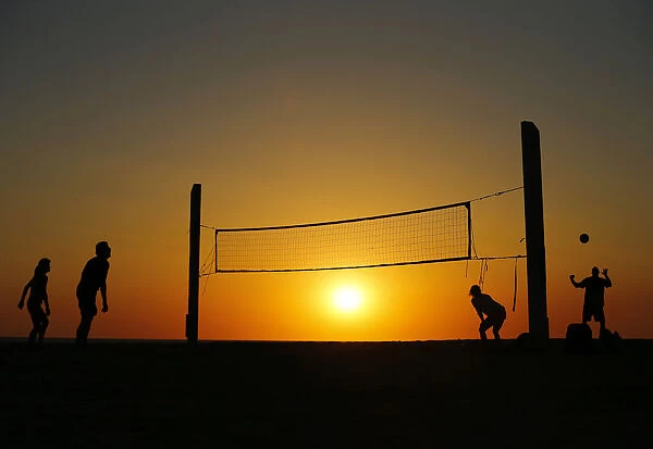 Beachgoers play volleyball at the beach as the sun sets in Carlsbad, California