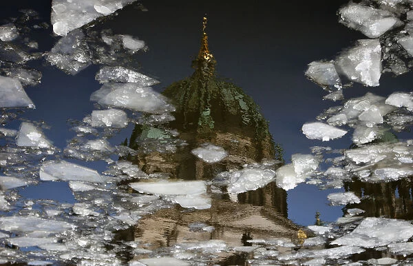 The Berlin Cathedral is reflected in Spree river that carries ice floats downstream