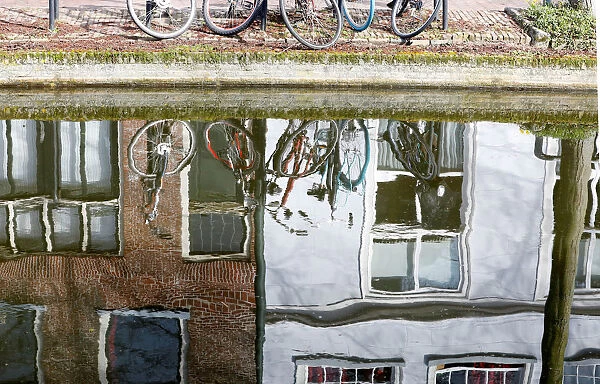 Bicycles are seen reflected in the water of a canal in Delft