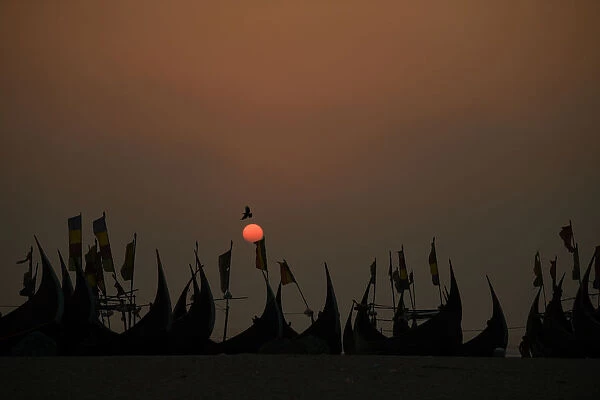 A bird flies past fishing boats at sunset on Shamplapur beach near a Rohingya refugee