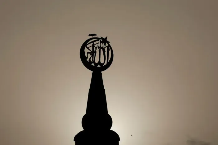 Framed Print : A bird sits on a religious sign on a mosque, silhouetted against the setting sun in Framed Print : A bird sits on a religious sign on a mosque, silhouetted against the setting sun in