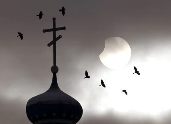 Birds fly past an Orthodox church during a partial solar eclipse in the town of Volozhin