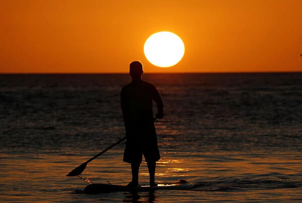 A boatman stands on a surfboard during sunset at Boracay in the Philippines