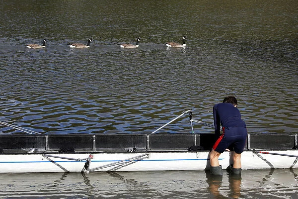 A boy adjusts his boat as geese swim past at Putney on the River Thames