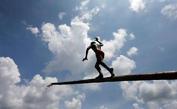 A boy climbs up a greasy pole in a climbing competition at a part of Sinhala