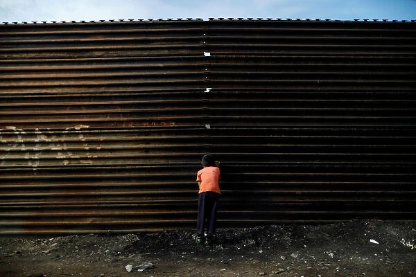 A boy looks through a hole in the current U. S. -Mexico border fence