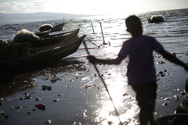 A boy plays with a stick next to row boats anchored on the shore in Port-au-Prince