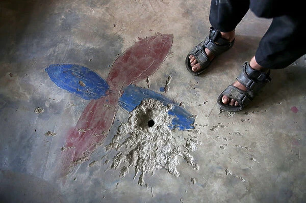 A boy stands next to a crater on the floor of his house