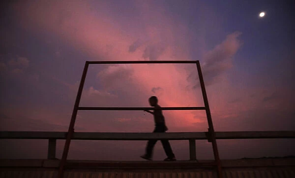 A boy walks past a structure being set up on a bridge to block the view of those passing