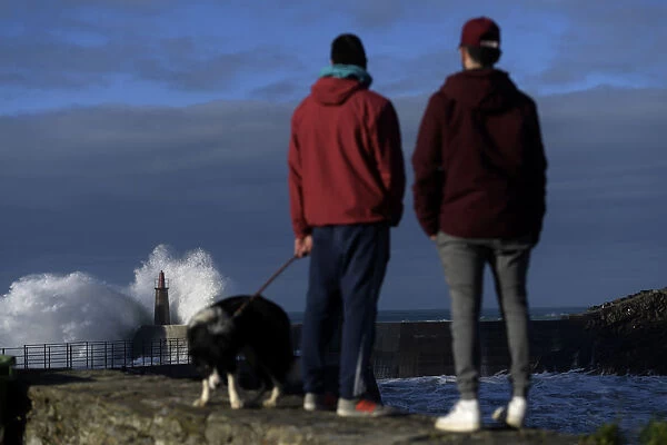 Two boys look at waves as they crash against a lighthouse in the port town of Viavelez