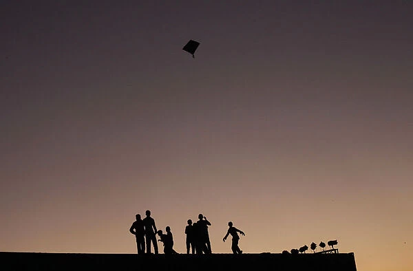 Boys are silhouetted against the setting sun as they fly a kite in Karachi