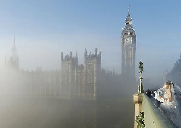 A bride poses for a photograph on Westminster Bridge as the fog clears in central London