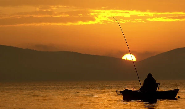 A Bulgarian fisherman rows his boat during the early morning at a lake south from Sofia