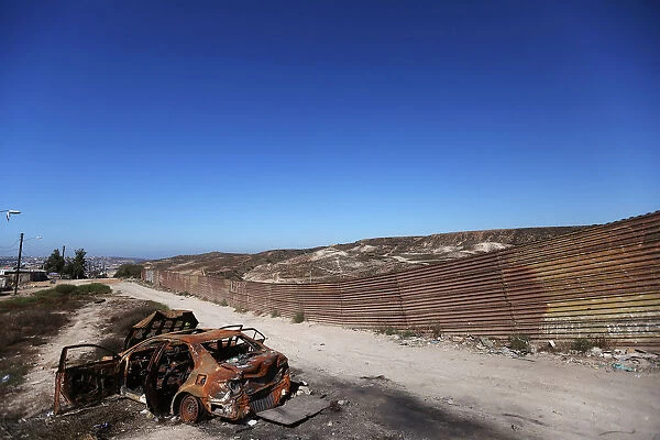 A burnt car is seen next to a section of the wall separating Mexico and the United States