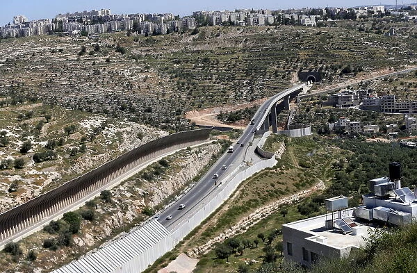 Cars drive on a road where workers construct a section of the controversial Israeli