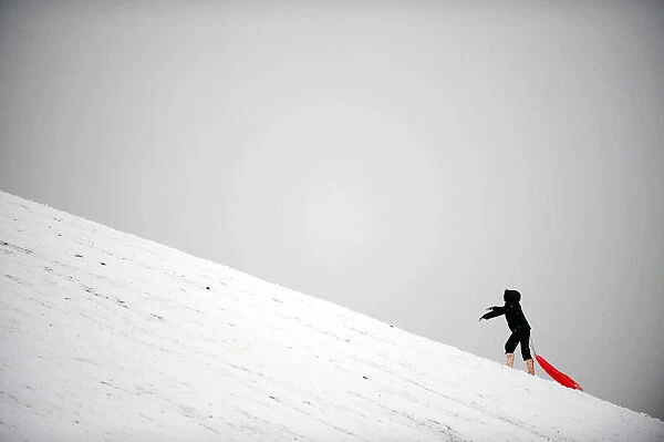 A child climbs a hill while sledging in the snow in London