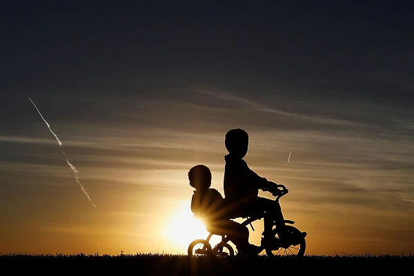 Children are seen in silhouette riding a tricycle along the Mississippi River Park at