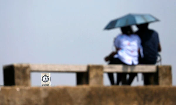 A clock tower is seen through a bench, as a couple rests on top of the Galle Dutch Fort