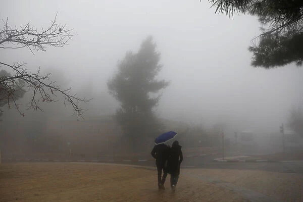 A couple holds an umbrella as they walk on the street on a foggy day in Jerusalem