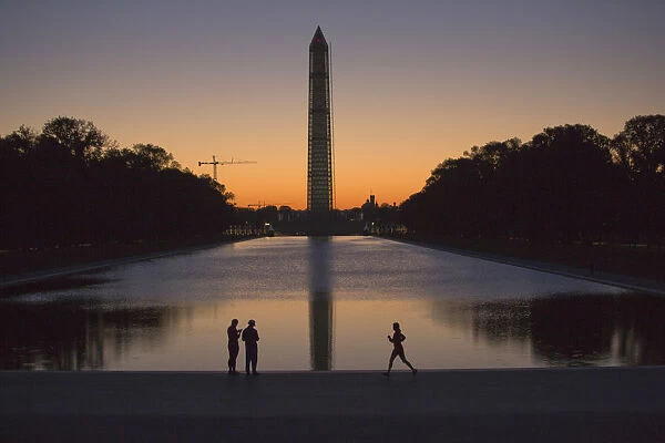 A couple and a jogger pass by the Lincoln Memorial Reflecting Pool before sunrise