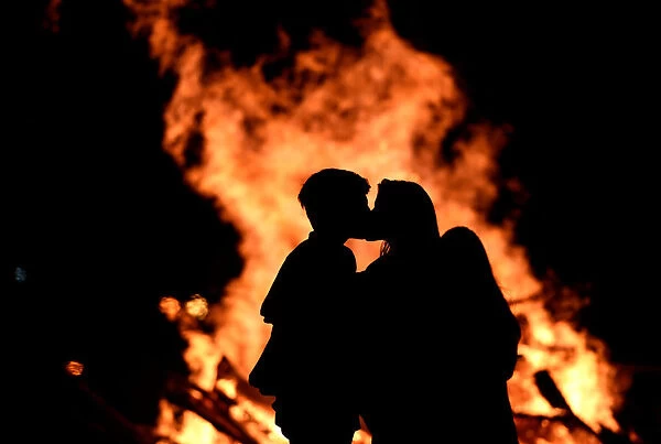 A couple kiss next to of the bonfire on the Poniente beach celebrating the summer