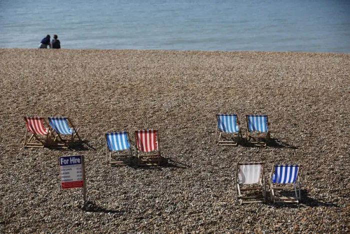Framed Print : A couple sit on the beach near deck chairs in the sunny weather on Brighton beach Framed Print : A couple sit on the beach near deck chairs in the sunny weather on Brighton beach
