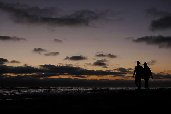 A couple walk hand in hand along the beach after sun set in Encinitas, California