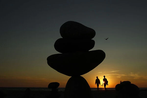 A couple walk past stone sculptures built on Moshup Beach as the sun sets in Aquinnah