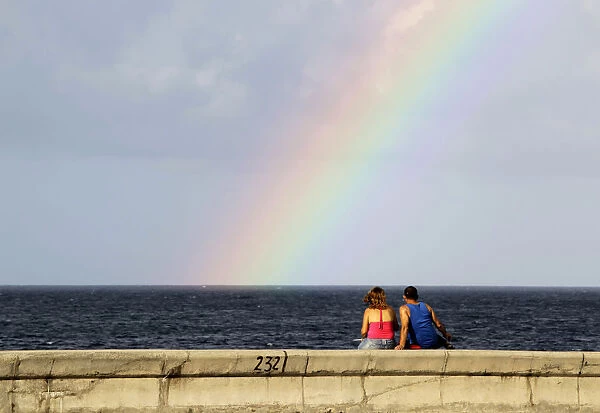 A couple watches a rainbow from Havanas seafront boulevard El Malecon