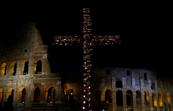A cross lit up with candles is seen in front of the Colosseum before the Via Crucis