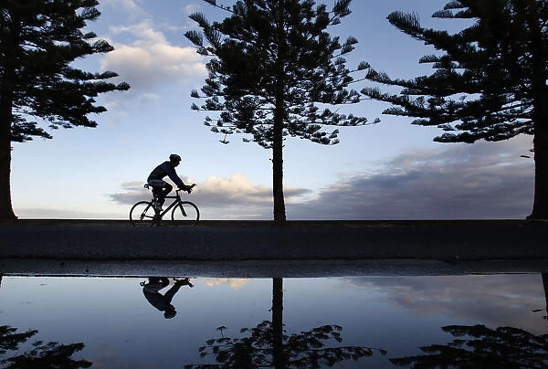 A cyclist is seen reflected while riding along a beach in Melbourne