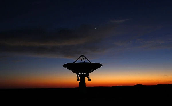 Dawn breaks over a radio telescope dish of the KAT-7 Array pointing skyward at the