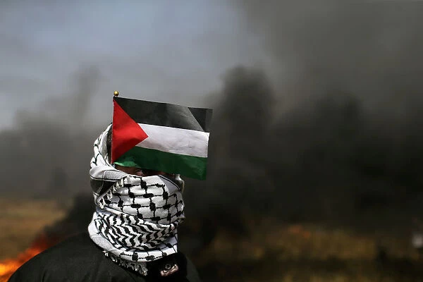 Demonstrator with a Palestinian flag looks on during clashes with Israeli troops at the