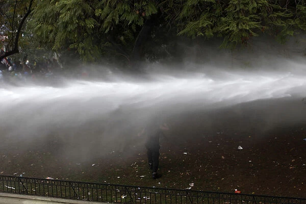A demonstrator runs away from a jet of water during a 48-hour national strike at Santiago