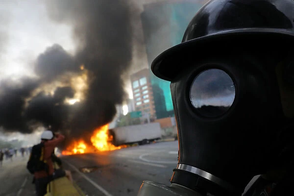 Demonstrators stand near burning trucks while rallying against President Nicolas Maduro