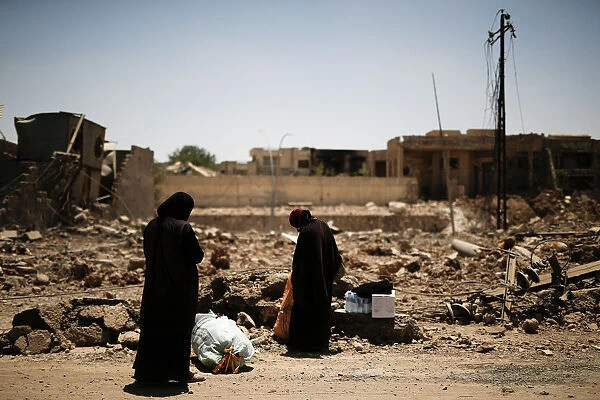 Two displaced Iraqi women stop to arrange their belongings as they flee from western